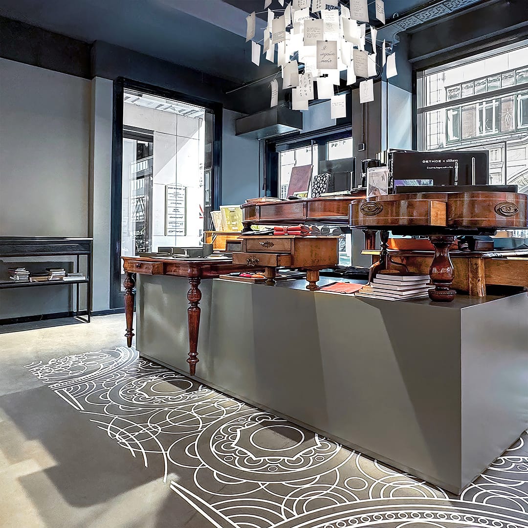 BEING BORN – Bethge Shop Hamburg: grafisches Teppichmuster & schwebende antike Tische Bethge Shop Hamburg – Retail Design von BEING BORN mit grafisch umgesetztem Teppichmuster, antiken Tischen, kubischen Formen und Zettel’z Pendelleuchte von Ingo Maurer.