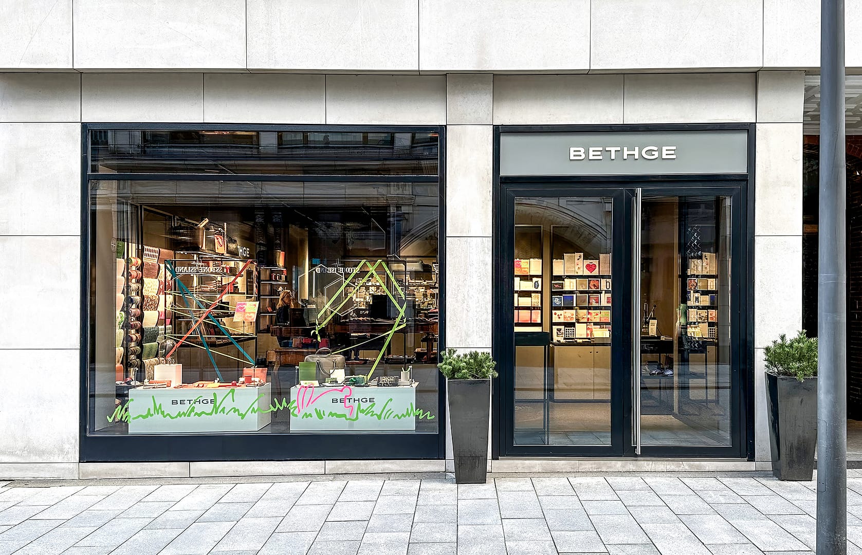 BEING BORN – Bethge Shop Hamburg: Schaufenster mit Lederwaren und grauen Kuben mit Logo Bethge Shop Hamburg – Retail Design von BEING BORN mit Lederwaren und Schreibaccessoires auf grauen Kuben mit Logo, im Schaufenster markant präsentiert.